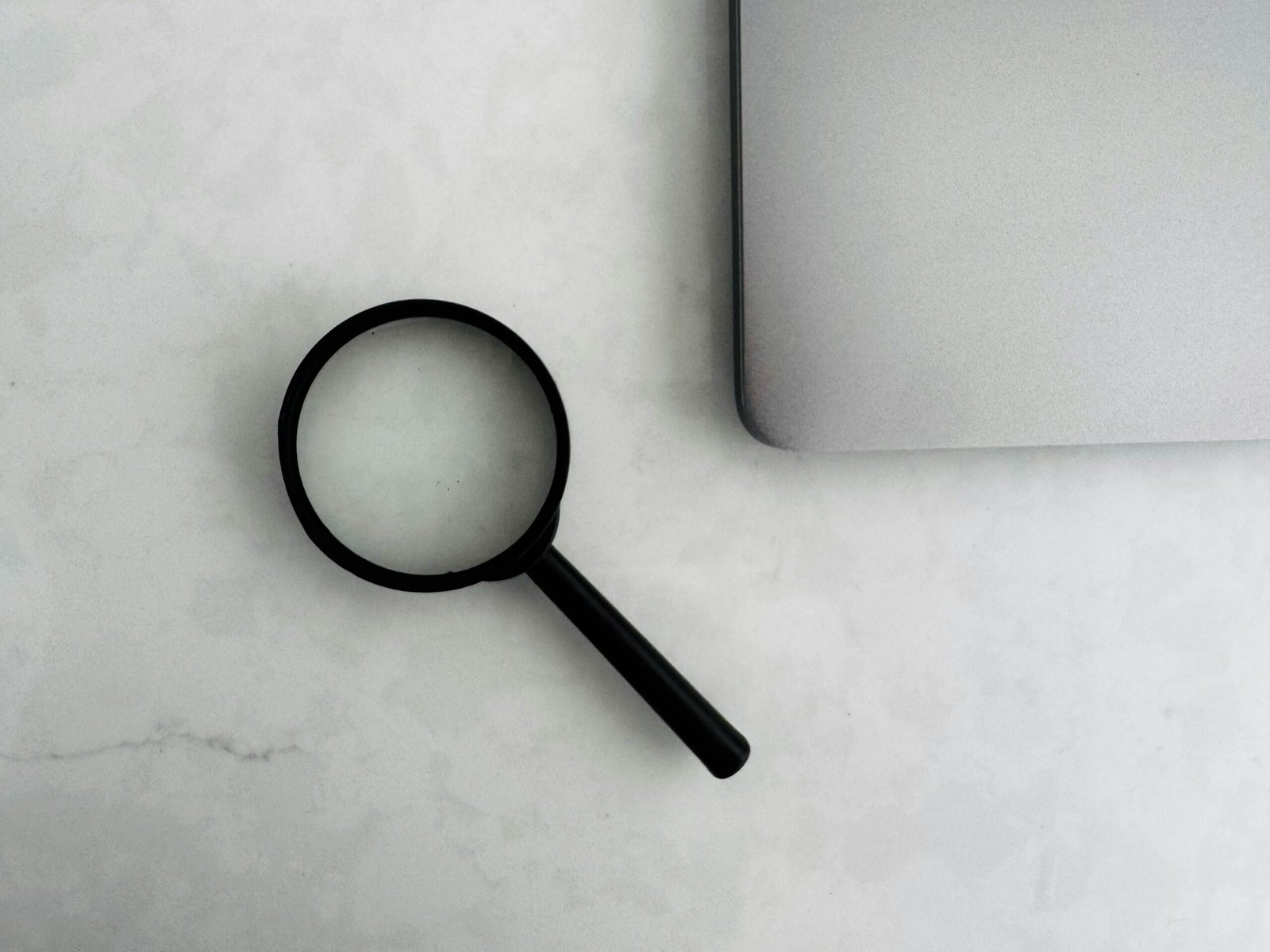 Magnifying glass next to a laptop, representing closely comparing trade calculator methodologies