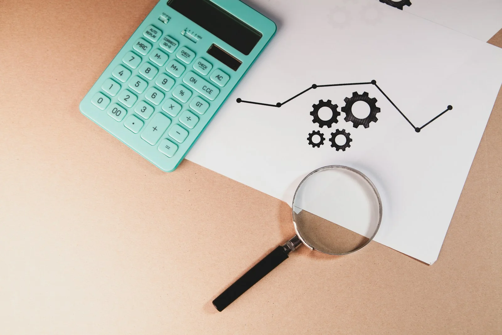 A calculator and a magnifying glass on a desk next to a hand-drawn trend chart, representing the difference between a trade calculator and a trade analyzer